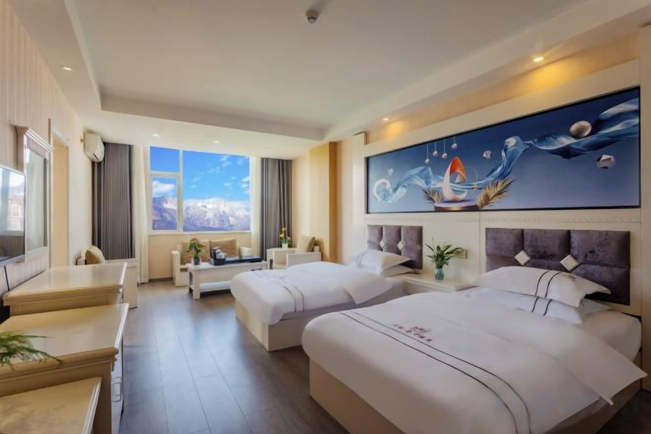A hotel room with two beds, a desk, a sofa, a TV, and a large window with a mountain view.