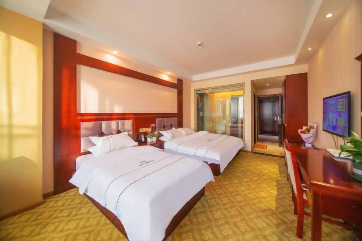 A hotel room with two beds, a desk, a chair, a television, and a door leading to a balcony.