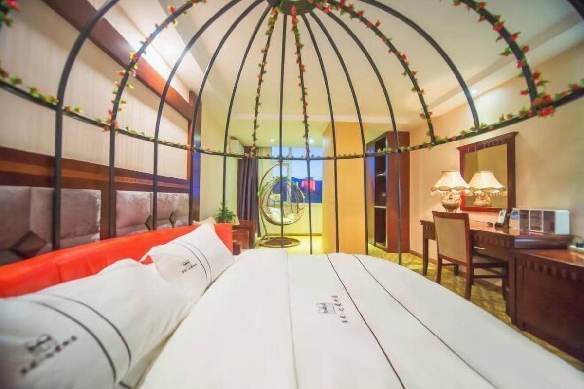 A hotel room with a bed, a desk, and a chair. There is a decorative ceiling with flowers.