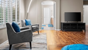Un salón moderno con un sofá gris, un televisor sobre un mueble negro y suelo de madera.
