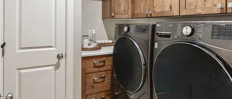 A laundry room with two front-loading washing machines, wooden cabinets above, and a white door.