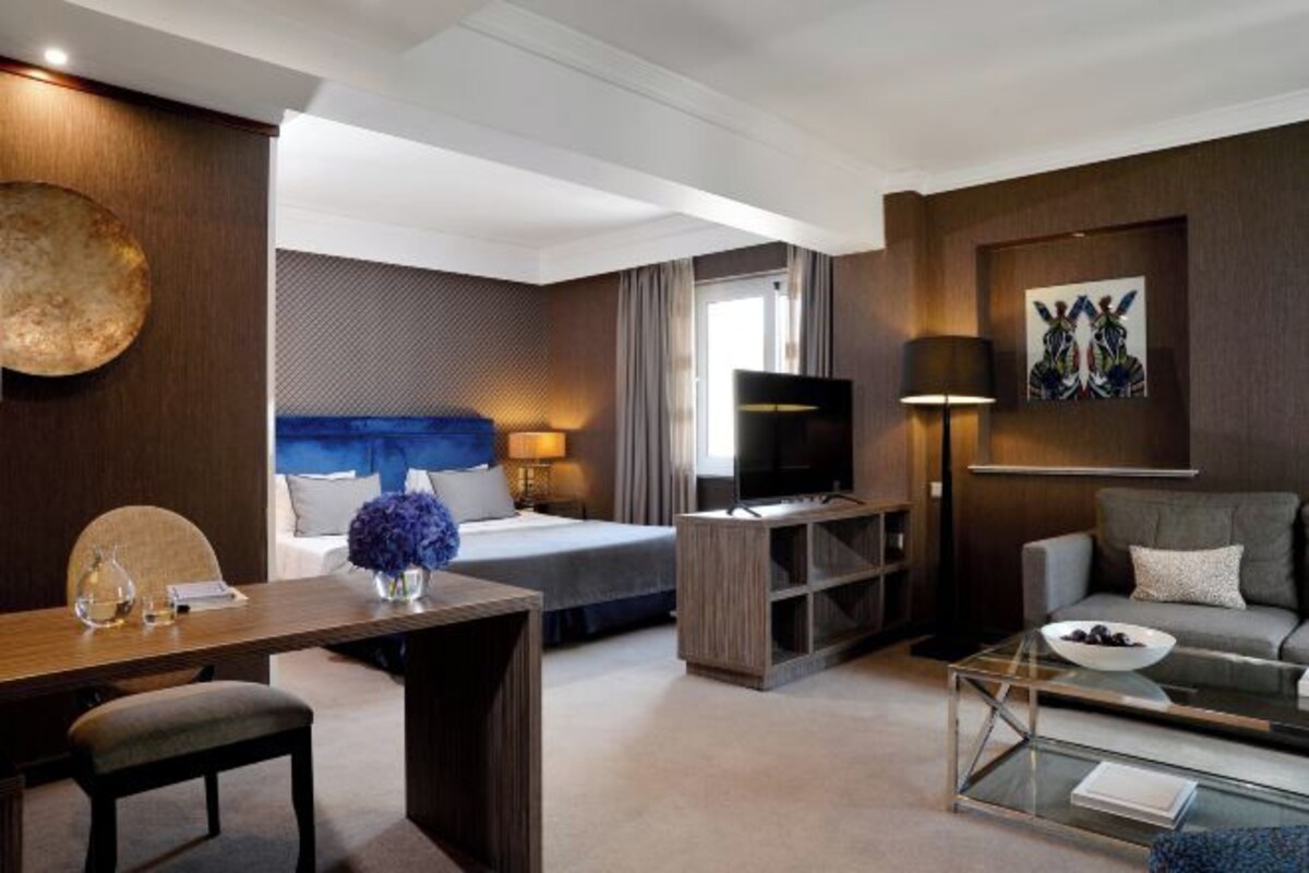 A hotel room with a bed, a TV, a sofa, a coffee table, and a desk with a lamp.