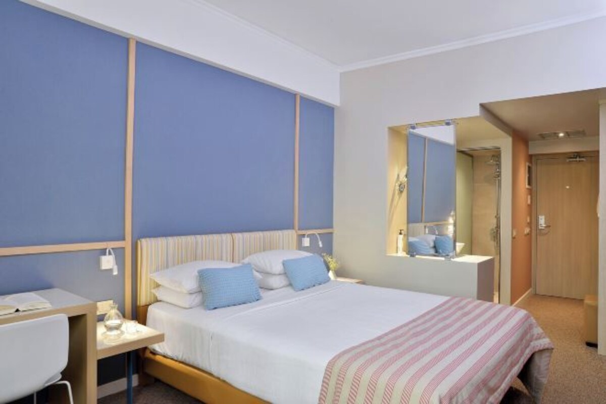 A hotel room with a bed, bedside table, and a mirror.