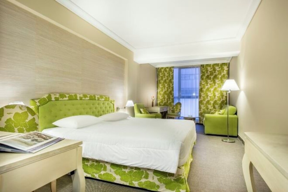 A hotel room with a large bed, a desk, a chair, and a small table.