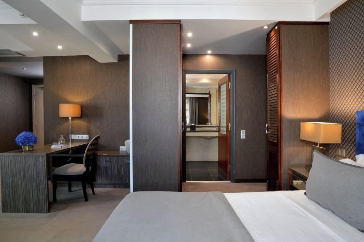 Una habitación de hotel moderna con cama, escritorio, silla y un baño visible a través de una puerta abierta.