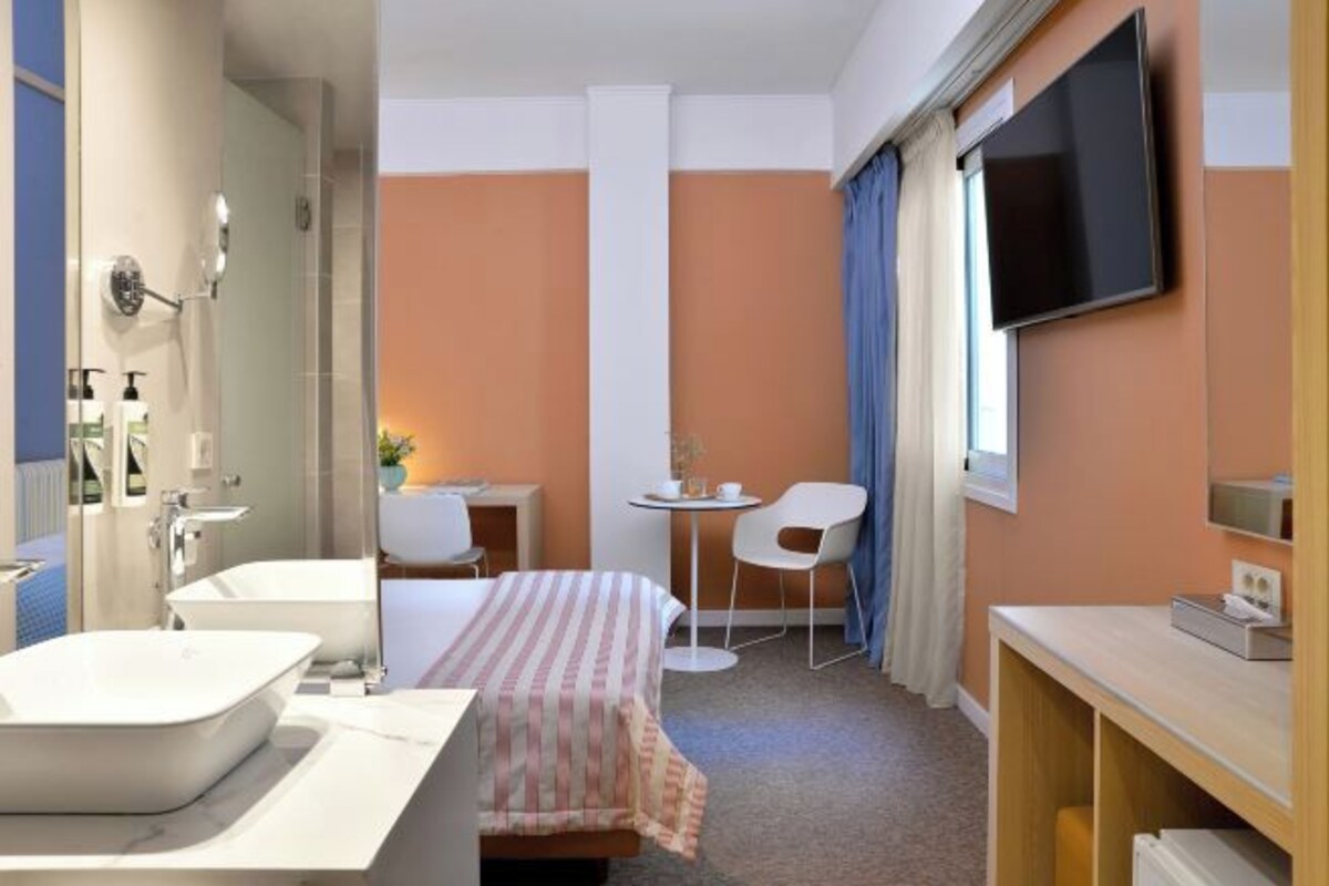 A hotel room with a bed, a large window, a TV, a desk, a chair, and a bathroom with a bathtub and sink.