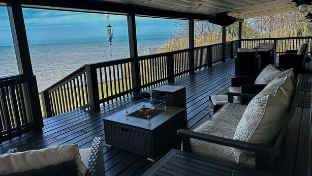 Eine überdachte Terrasse im Freien mit Blick auf das Meer, möbliert mit Korbmöbeln und einem Tisch.