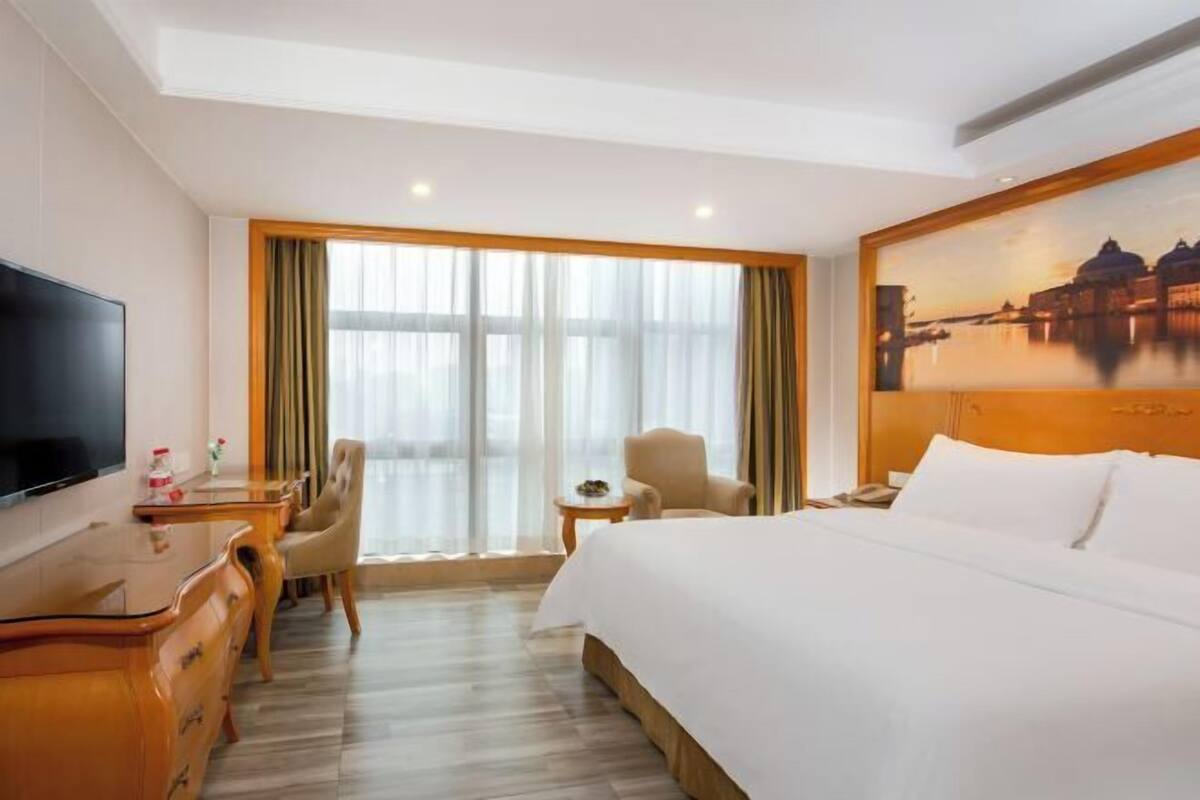 A hotel room with a bed, a desk, a chair, a television, and a large window with curtains.
