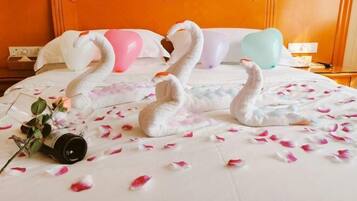 A hotel room with a bed featuring swan-shaped pillows, a bedside table with a lamp, and a decorative vase with flowers.