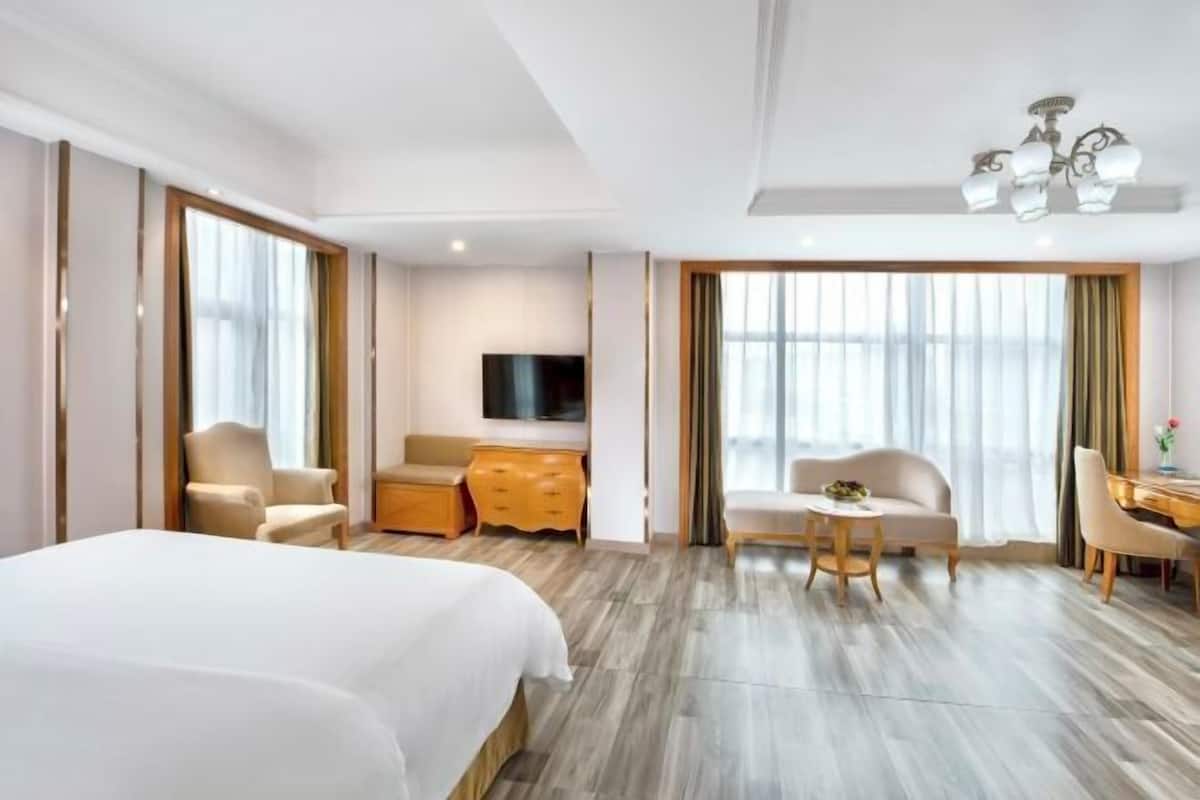 A hotel room with a large bed, a desk, a chair, a television, and a chandelier.