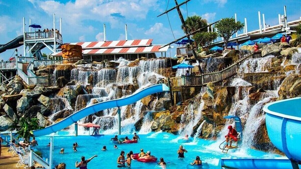A water park with a large pool, multiple slides, and a waterfall. - Luxurious Condo with Zero Entry Pool & Gated Beach (Miramar Beach)