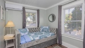 A cozy room with a grey sofa bed, a small table with a lamp, and a window with blinds. - ArtSea2. 2BR · Upstairs w/Ample Parking | Near Beaches & LECOM (Bradenton)