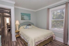 A bedroom with a bed, a nightstand, a lamp, a painting, and a window with blinds. - ArtSea2. 2BR · Upstairs w/Ample Parking | Near Beaches & LECOM (Bradenton)