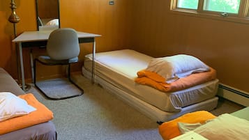 Et lille hotelværelse med skrivebord, stol, to enkeltsenge, et lille bord og et vindue med udsigt til træer.