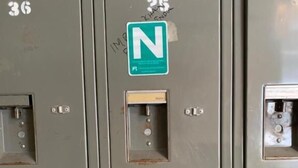 Une rangée de casiers métalliques portant les numéros 36 et 25, un panneau vert avec la lettre « N », et un petit panneau de commande.