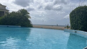 Piscina límpida com borda em azulejo, rodeada por vegetação e vista para a praia.