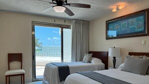 A hotel room with two beds, a ceiling fan, a view of the beach, and a painting on the wall. - Cancun Ocean Front Family Villa 18  at Villas Nizuc (Cancun)