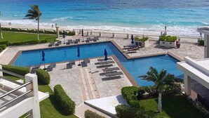 A resort pool area with two swimming pools, lounge chairs, and a view of the ocean. - Cancun Ocean Front Family Villa 18  at Villas Nizuc (Cancun)