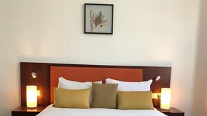 Un lit bien fait, avec une literie blanche et beige, deux lampes de chevet et un tableau encadré au mur.