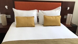Un lit bien fait, avec des oreillers blancs et moutarde, un plaid marron et une tête de lit en bois.