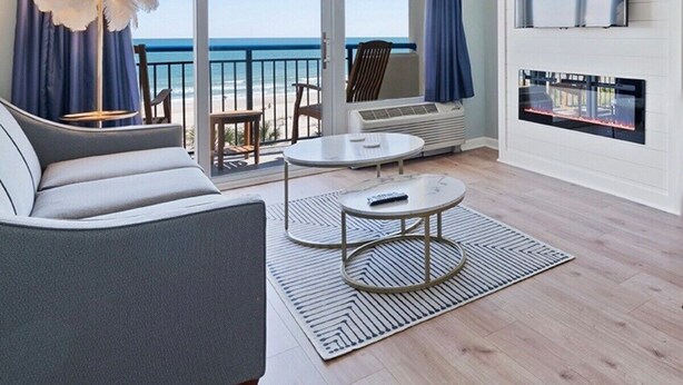 Un soggiorno moderno con un divano, un tavolino da caffè e una TV. È presente un balcone con vista sull'oceano.