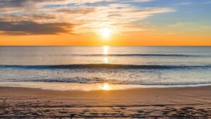 Una spiaggia con un tramonto sull'oceano, onde calme e cielo sereno.