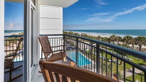 Un balcone con sedie in legno, una piscina e vista sulla spiaggia e sull'oceano.