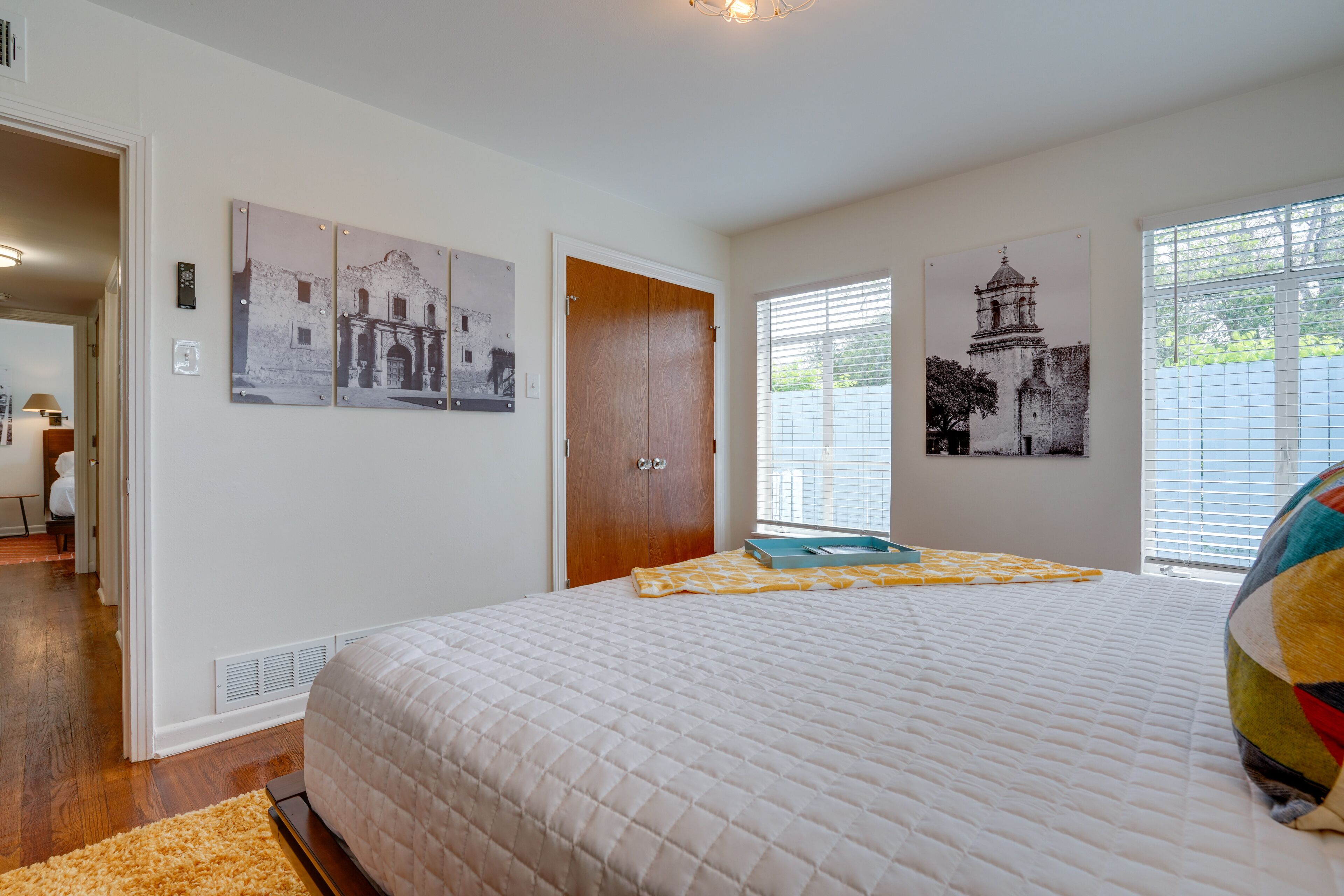A bedroom with a large bed, a wooden door, and two windows with blinds.