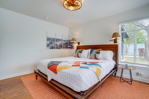 Ein Schlafzimmer mit einem hölzernen Bett, Blick ins Freie durch ein Fenster und einem an der Wand hängenden Bild.
