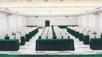 A conference room with rows of tables and chairs, a stage at the front, and a green carpet.