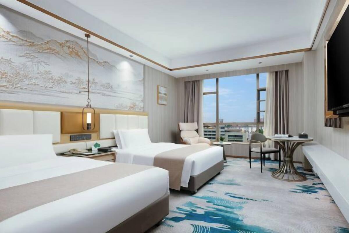 Habitación de hotel con dos camas, un escritorio, una silla, televisión y un ventanal con vistas a la ciudad.