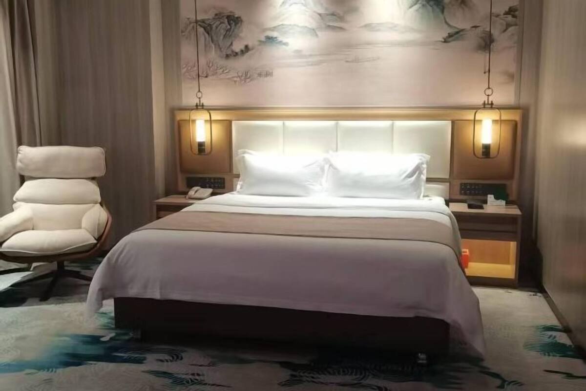Una habitación de hotel con una cama grande, una silla, una mesita de noche y una lámpara de pared.