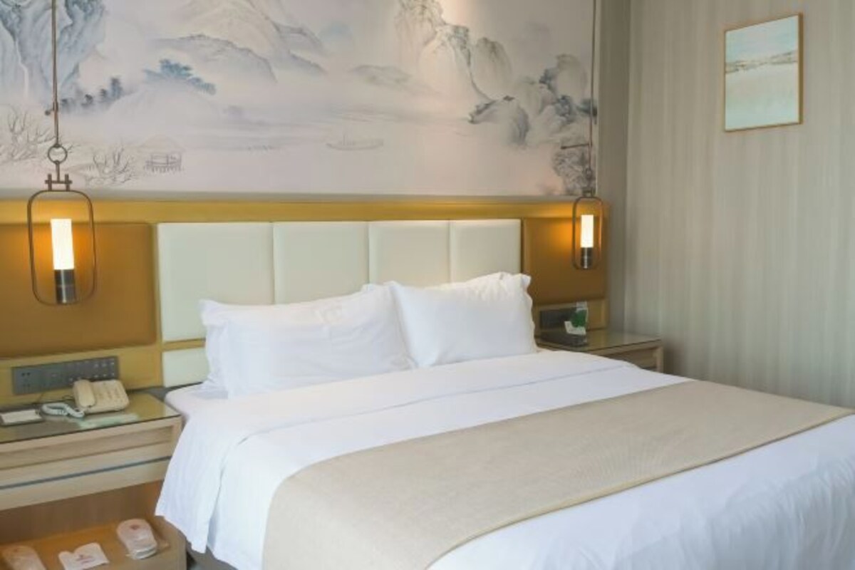 Habitación de hotel con una cama grande, una mesita de noche con teléfono y una pared decorada con un cuadro.