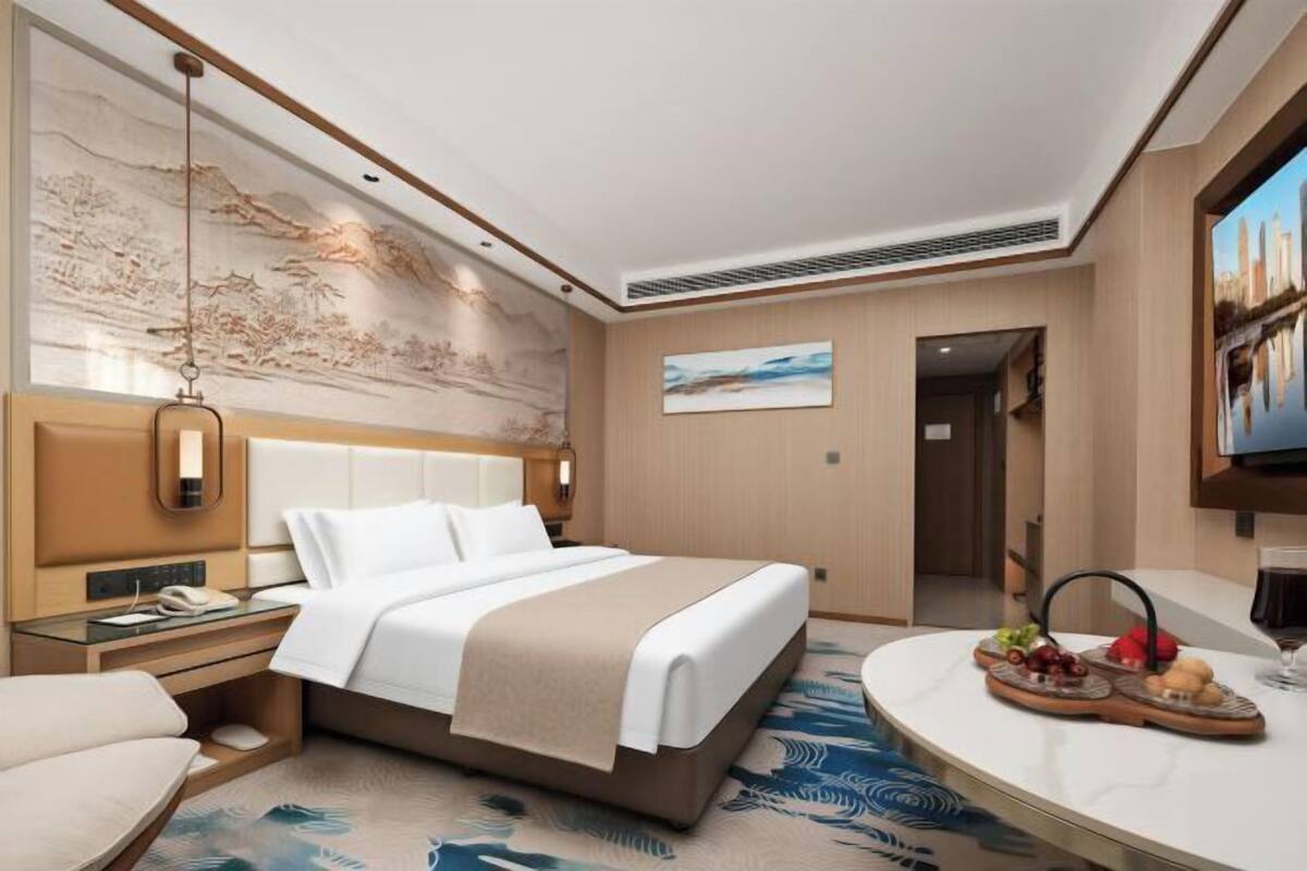 Habitación de hotel con cama, mesita de noche, lámpara, obra de arte y una zona de comedor con mesa y sillas.