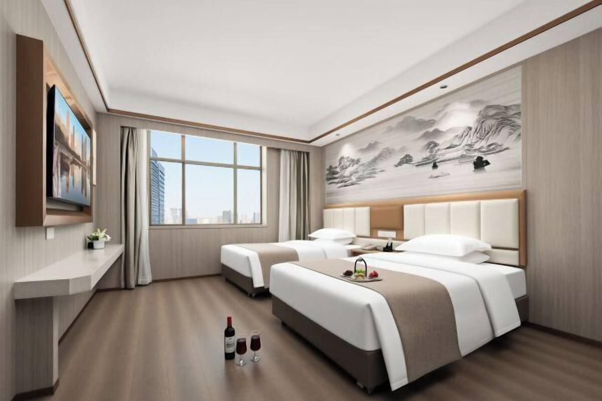 Una habitación de hotel con dos camas, un ventanal grande, un cuadro en la pared y un televisor a la izquierda.