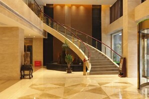 Un vestíbulo de hotel con una imponente escalera, suelo de mármol y una mesa de recepción.