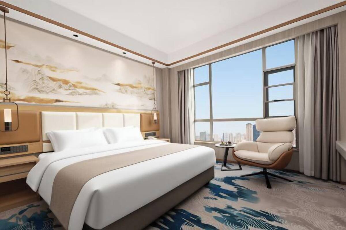 Una habitación de hotel moderna con una cama grande, un área de descanso y vistas a la ciudad.