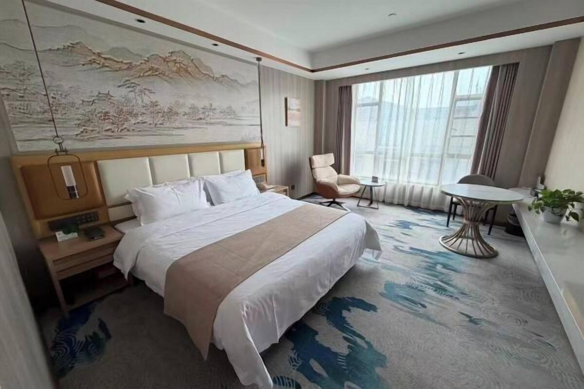 Una habitación de hotel con una cama grande, un escritorio, una silla, una mesita y un cuadro en la pared.