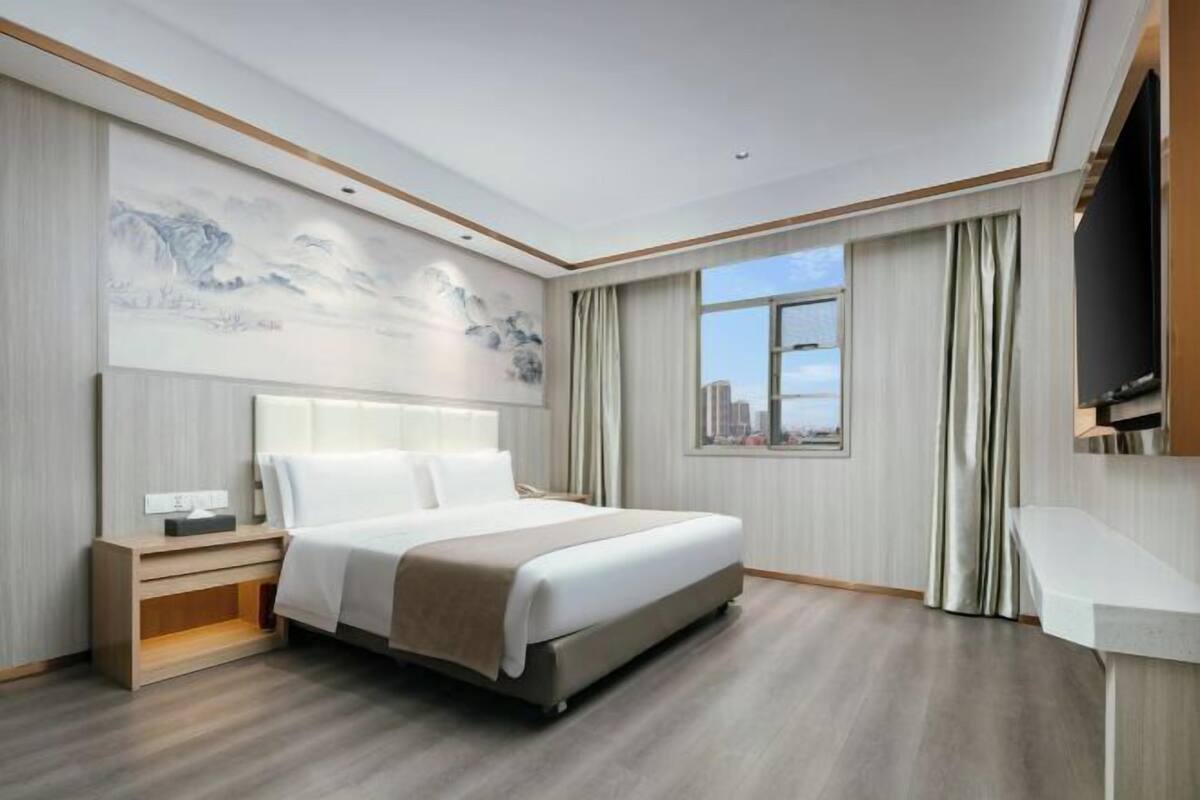 Habitación de hotel moderna con una cama grande, una mesita de noche, un escritorio y vistas a la ciudad por la ventana.