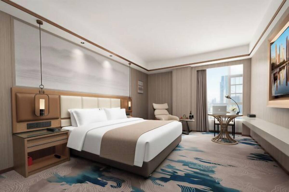 Habitación de hotel con una cama grande, mesitas de noche, un escritorio y vistas a la ciudad.