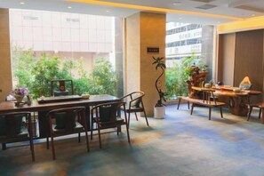 A hotel dining area with a table set for four, a potted plant, and a view of greenery outside.