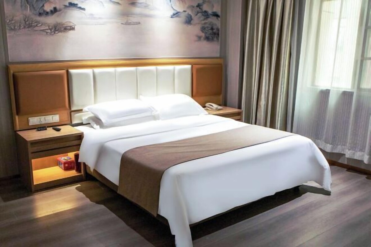 A hotel room with a large bed, a bedside table with a phone, a nightstand with a lamp, and a painting on the wall.