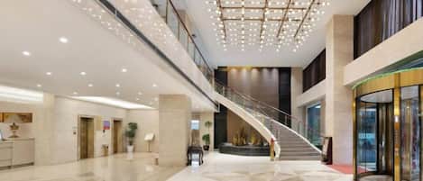 A spacious lobby with a central staircase, polished floors, and modern lighting fixtures.