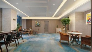 A spacious hotel lobby with a blue carpet, wooden furniture, and a large plant. - Huakang International Hotel (Qianjiang)