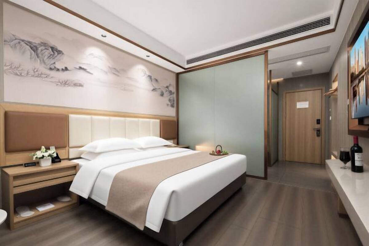 Una habitación de hotel moderna con una cama grande, mesitas de noche, una obra de arte colgada en la pared y una puerta corredera que da a un baño.