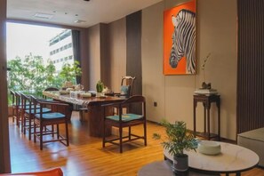 A dining area with a wooden table and chairs, a potted plant, and a painting on the wall. - Huakang International Hotel (Qianjiang)