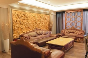 A room with a large, ornate wooden wall panel, leather sofas, and a wooden coffee table. - Huakang International Hotel (Qianjiang)