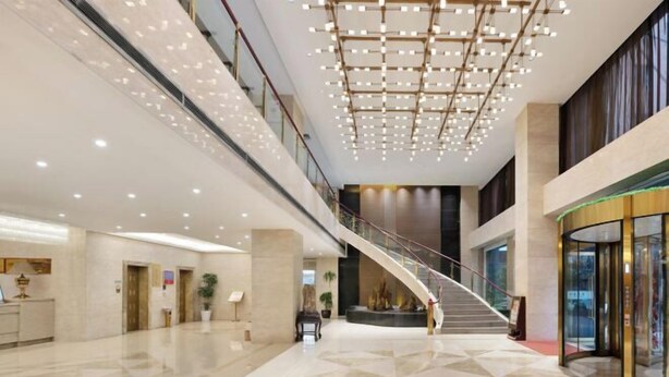 A spacious lobby with a high ceiling, a central staircase, and a reception desk. - Huakang International Hotel (Qianjiang)