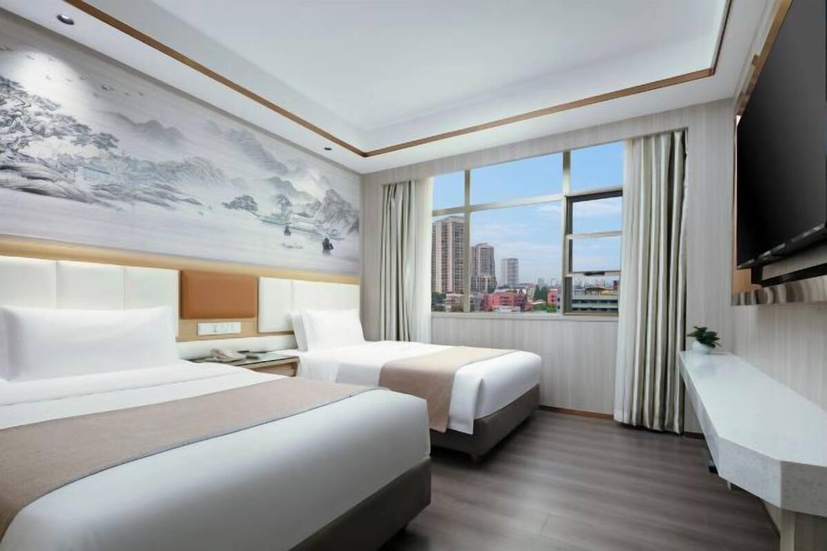 Habitación de hotel con dos camas, un ventanal con cortinas, un televisor de pantalla plana y un televisor montado en la pared.