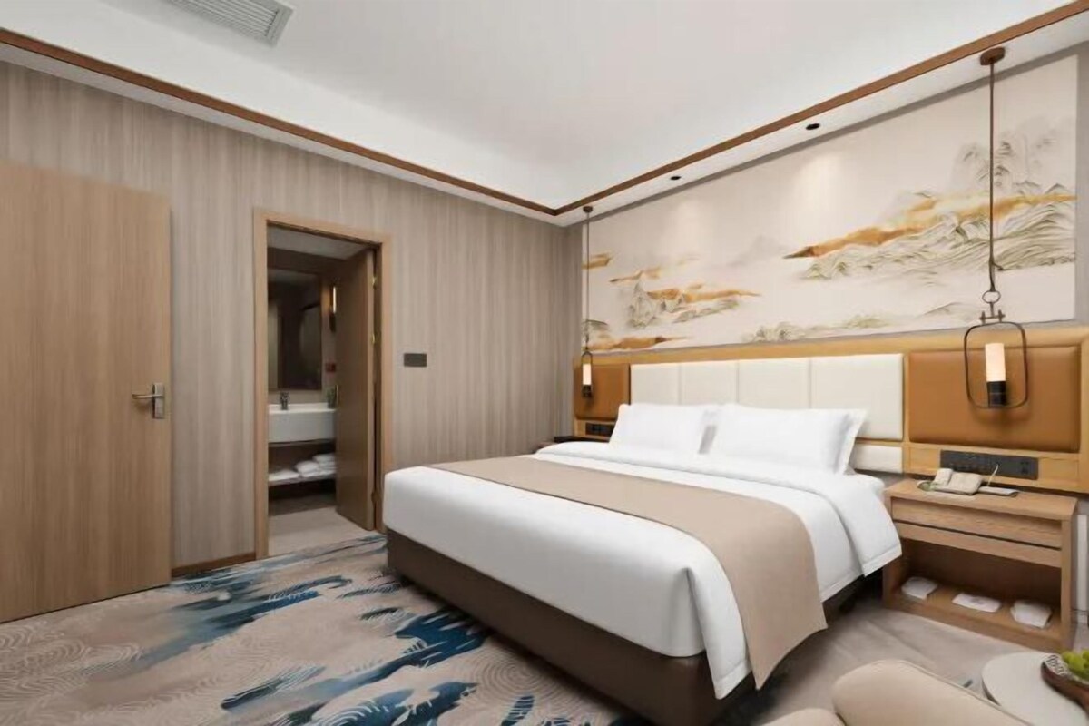A hotel room with a large bed, a bedside table, a nightstand, a wardrobe, and a painting on the wall.